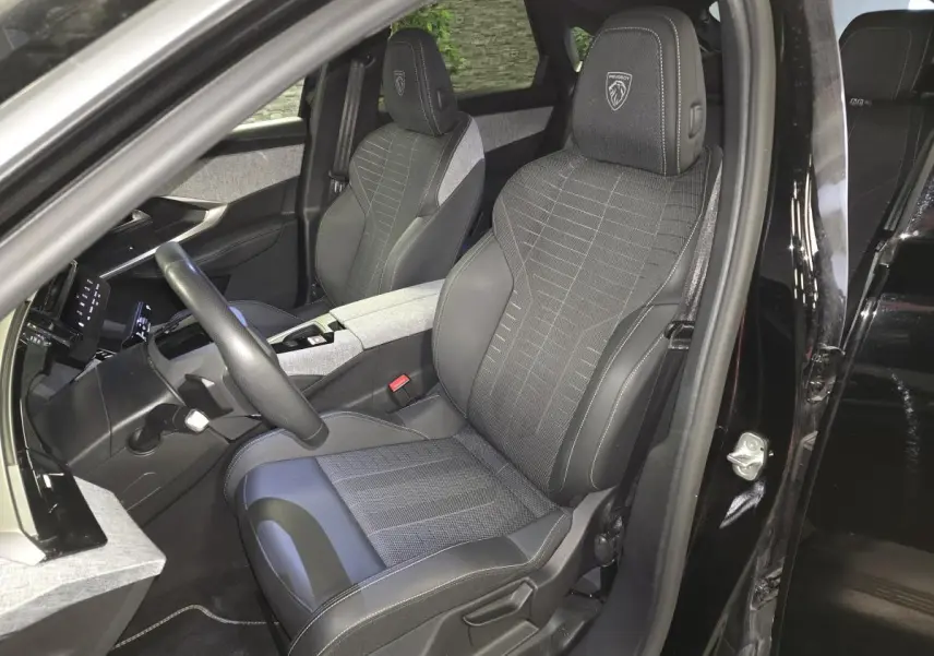 Vue intérieure côté conducteur du Peugeot 3008 Hybrid 2025 noir, sièges tissu et cuir avec logo Peugeot brodé.