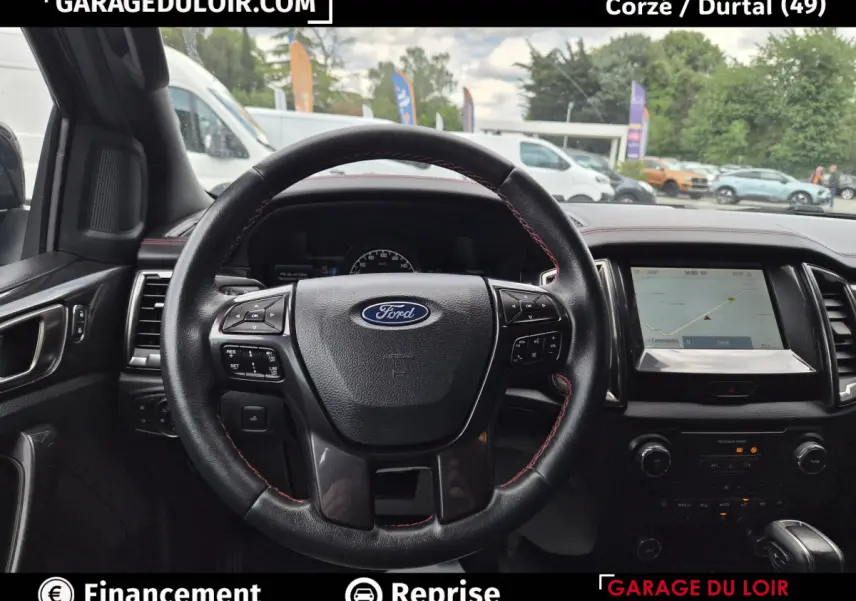 Vue intérieure centrée sur le volant cuir noir avec coutures rouges du Ford Ranger gris foncé, écran tactile et tableau de bord visibles.