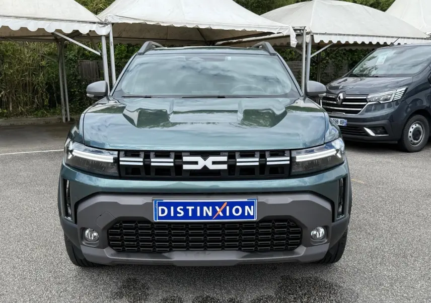 Vue avant d'un Dacia Duster Hybrid 140 Journey vert cèdre avec calandre noire et phares LED allumés.