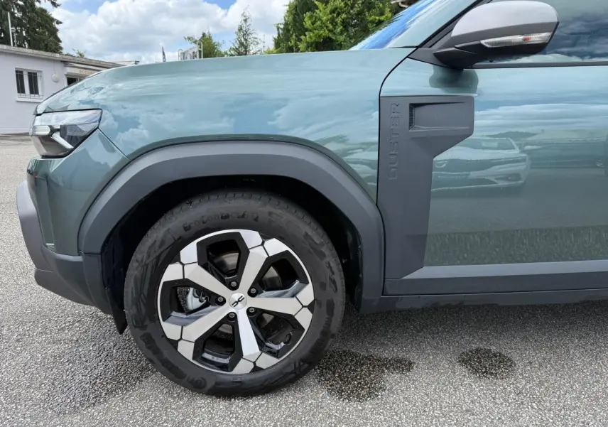 Vue de profil côté avant gauche du Dacia Duster Hybrid 140 Journey vert cèdre avec jante alliage et logo Duster sur l'aile.