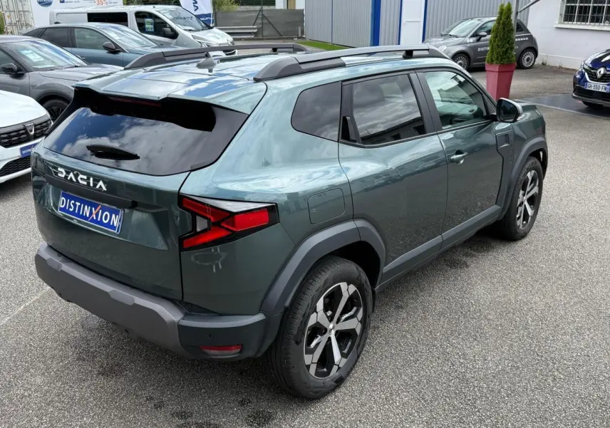 Vue 3/4 arrière droite du Dacia Duster Hybrid 140 Journey vert cèdre avec barres de toit et jantes noires.