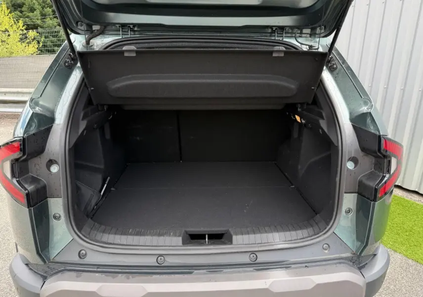 Coffre ouvert vu de l'arrière du Dacia Duster Hybrid 140 Journey vert cèdre, montrant un espace de chargement vide.