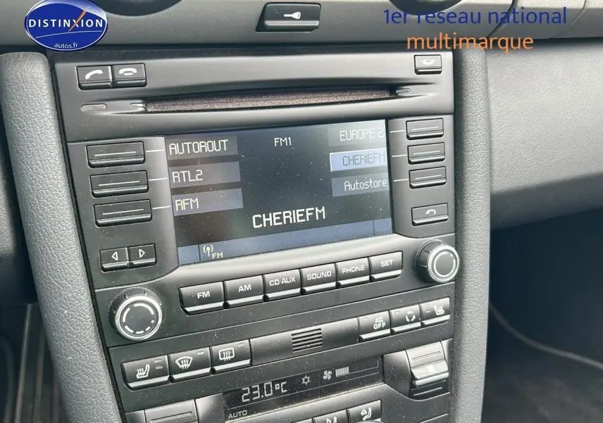 Vue rapprochée du tableau de bord noir de la Porsche Boxster 987 avec écran radio affichant la station CHERIE FM.