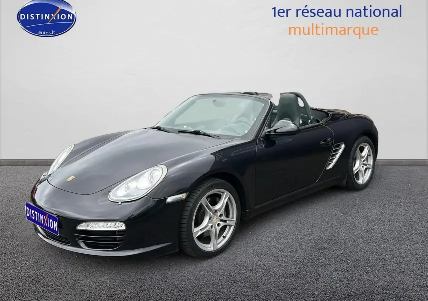 Porsche Boxster (987) noir vue 3/4 avant droit, capote ouverte, jantes alu 17 pouces et phares bi-xénon directionnels.
