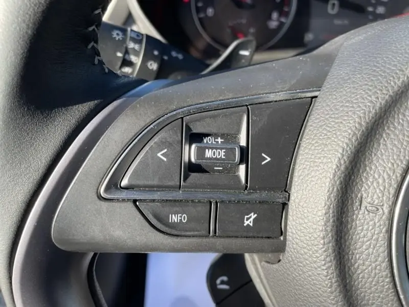 Gros plan sur les commandes audio au volant côté gauche d'une Suzuki Swift blanche 2025 1.2 Hybrid Pack Auto.