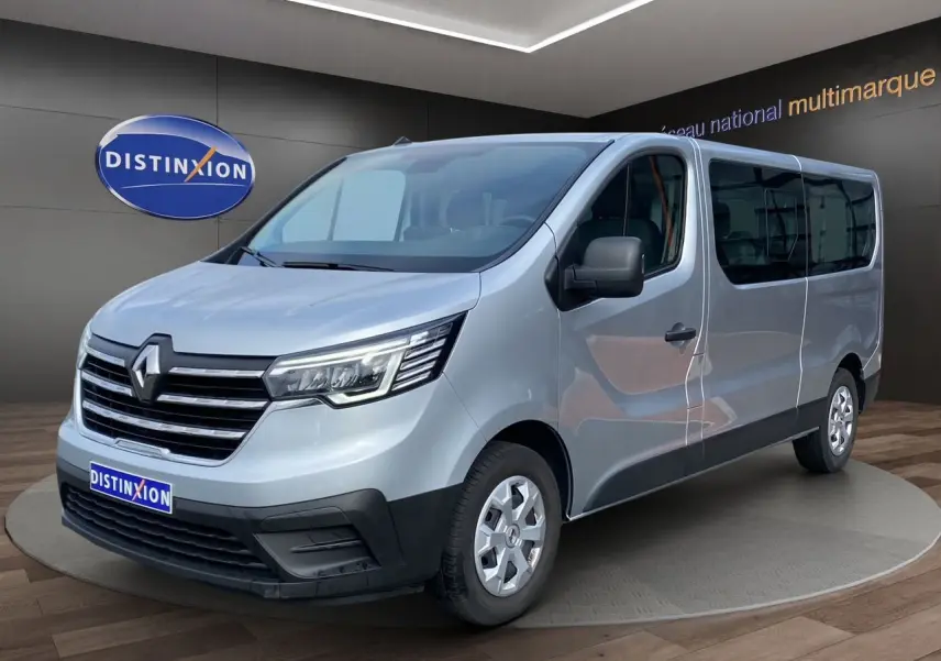 Vue 3/4 avant droit d'un Renault Trafic Combi gris platine 2023 avec calandre chromée et vitres teintées.