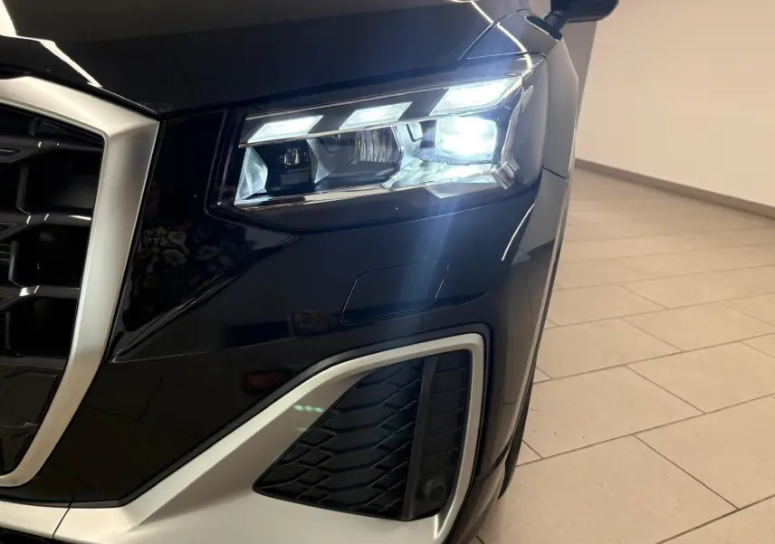Gros plan sur le phare avant droit allumé de l’Audi Q2 35 TFSI S Line noir mythic, avec calandre et détails argentés.