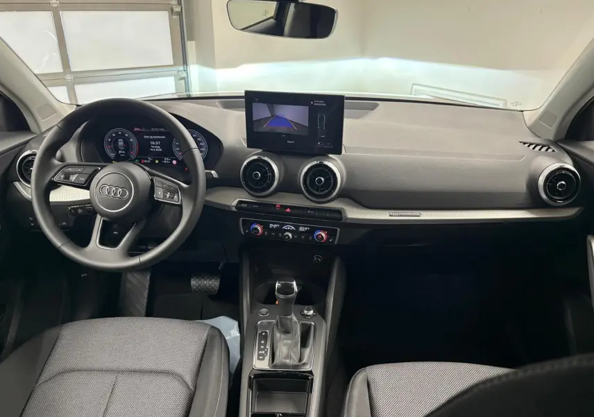 Vue intérieure de l'Audi Q2 35 TFSI S Line 2026, tableau de bord et console centrale avec écran et volant multifonctions.