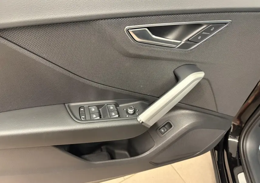 Gros plan sur la porte avant gauche de l'Audi Q2 Noir Mythic, montrant les commandes des vitres et la poignée intérieure argentée.