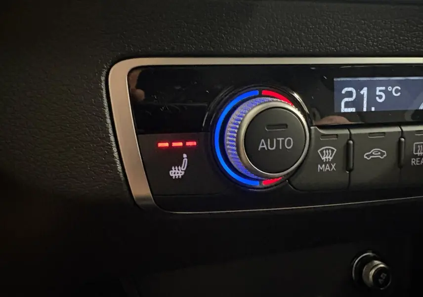 Détail du bouton de réglage de la climatisation avec fonction siège chauffant activée sur Audi Q2 Noir Mythic.