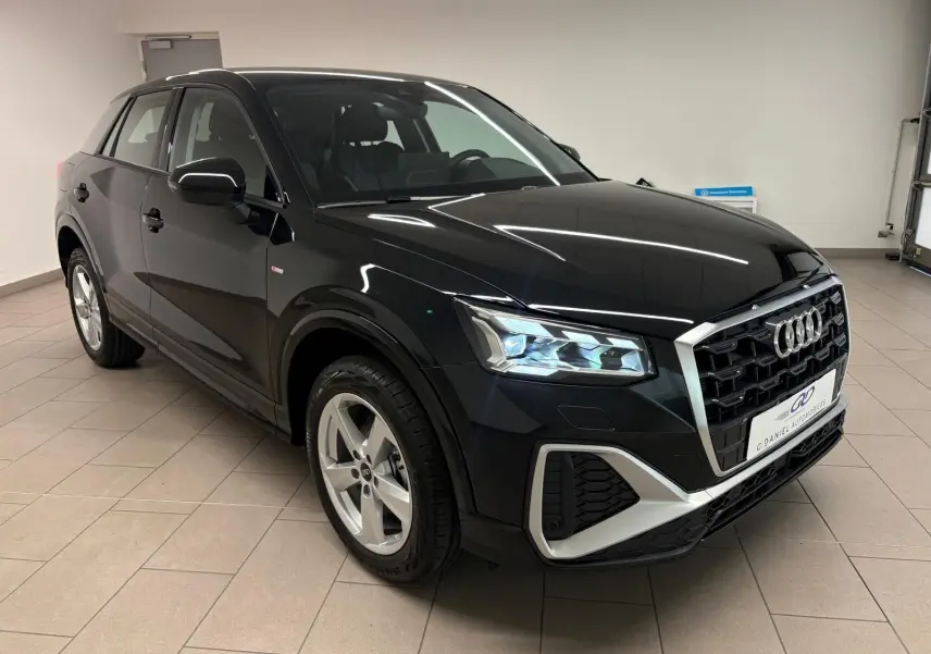 Audi Q2 35 TFSI S Line noir mythic en 3/4 avant droit, avec calandre large et feux LED allumés.