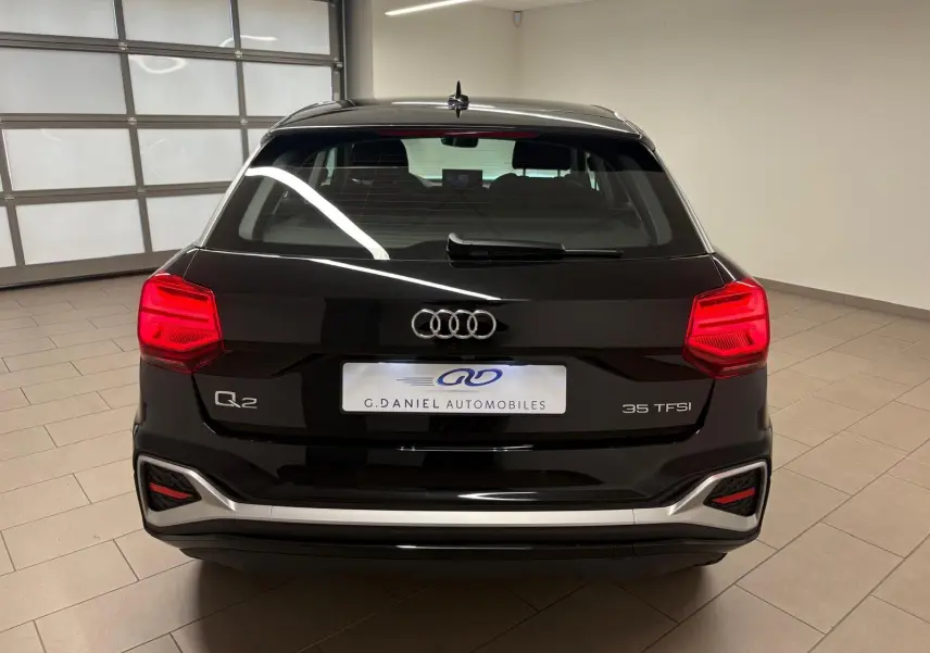 Vue arrière d'un Audi Q2 35 TFSI noir mythic avec feux rouges allumés dans un garage intérieur.