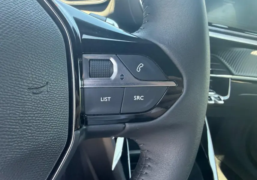 Gros plan sur les commandes gauche du volant noir du Peugeot 2008 Hybrid 136 e-DCS6 Style, avec tableau de bord en arrière-plan.