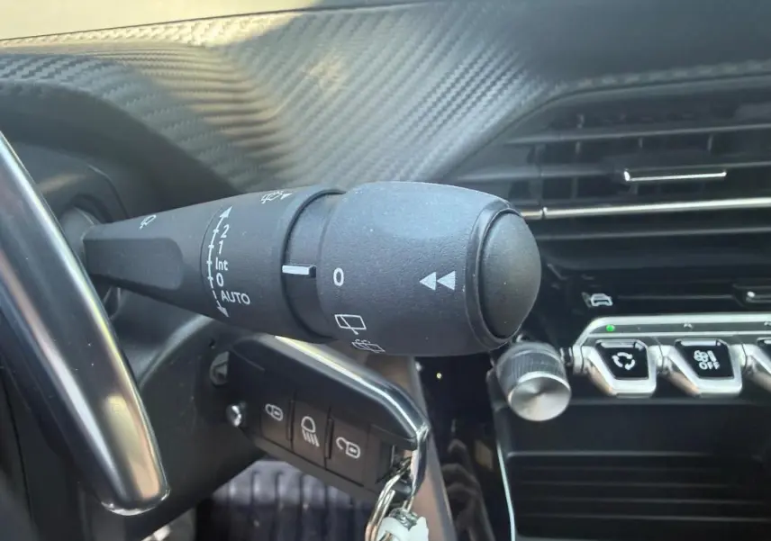 Gros plan sur la commande d’essuie-glace et la clé insérée dans le contacteur du Peugeot 2008 Hybrid noir, intérieur moderne.