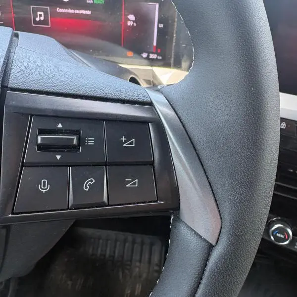 Gros plan sur le volant côté gauche de l'Opel Mokka électrique gris 2025 avec commandes audio et tableau de bord numérique.