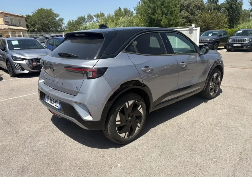 Vue 3/4 arrière droite de l'Opel Mokka électrique gris avec toit noir et jantes alliage 17 pouces sur parking.