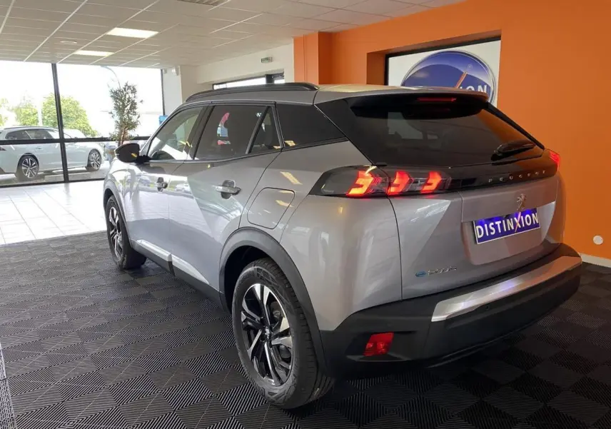 Vue 3/4 arrière droite du Peugeot 2008 e-136 Allure Pack gris Artense avec jantes bi-tons et vitres surteintées en showroom.