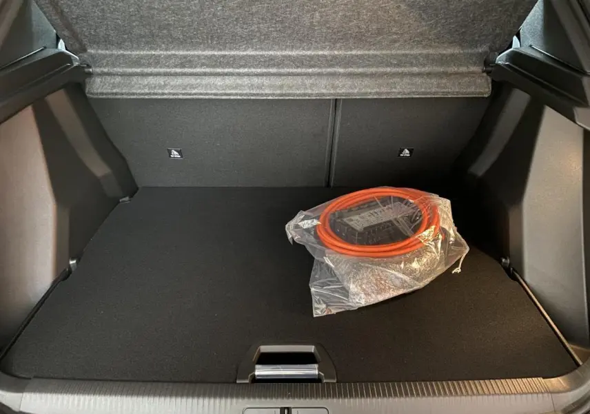 Coffre ouvert d'un Peugeot 2008 e-136 Allure Pack gris Artense avec câble de recharge électrique rangé sur le tapis noir.