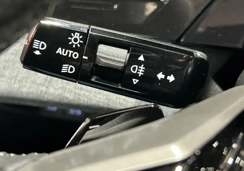 Gros plan sur la commande des feux automatiques et antibrouillard du Peugeot 5008 III Hybrid 145 GT, intérieur noir.