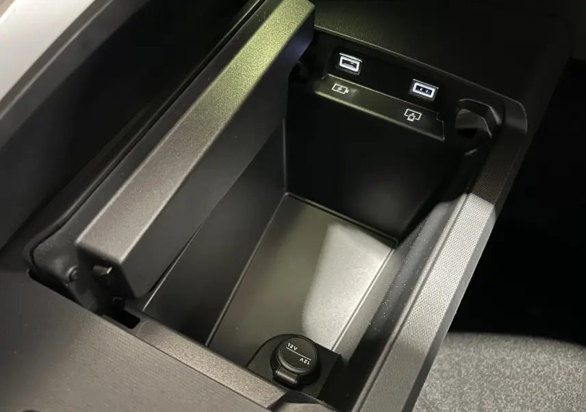 Vue rapprochée de la console centrale noire du Peugeot 5008 III Hybrid avec ports USB et prise 12V intégrés.