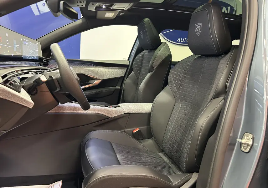 Vue intérieure côté conducteur du Peugeot 5008 Hybrid 2026, sièges noirs avec logo Peugeot et toit ouvrant panoramique visible.