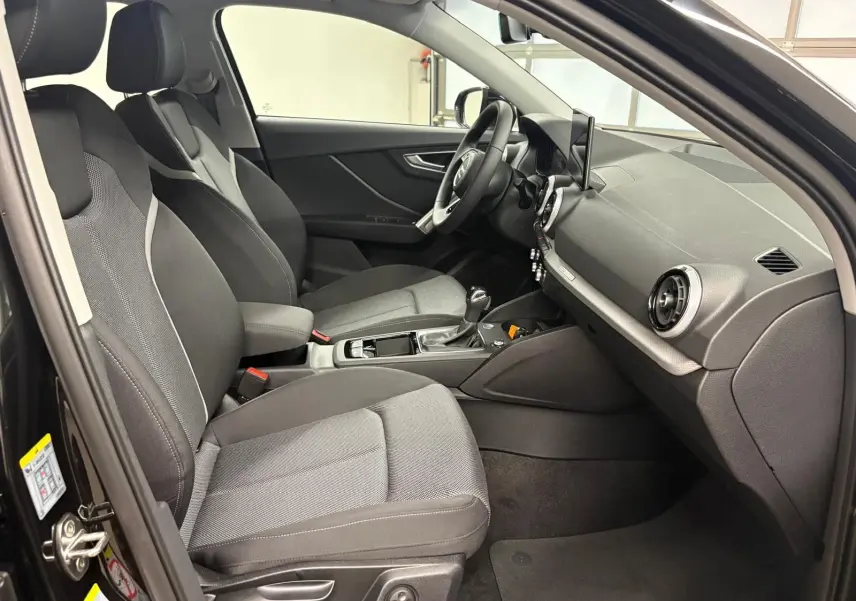 Vue intérieure côté conducteur de l'Audi Q2 35 TFSI S Line 2026 avec sièges tissu gris et tableau de bord noir.
