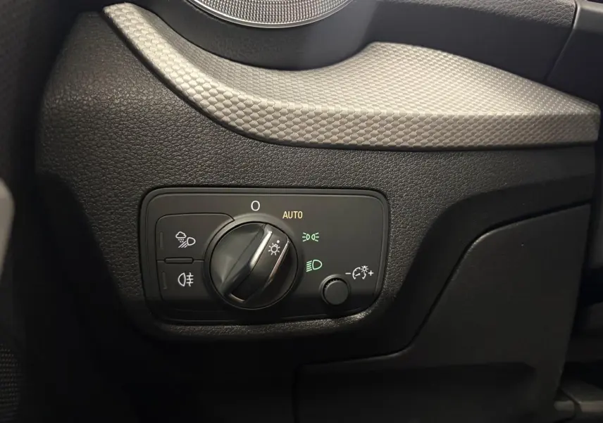 Gros plan sur le panneau de commande des phares à gauche du volant dans l’Audi Q2 35 TFSI 150 S Line noir Mythic.