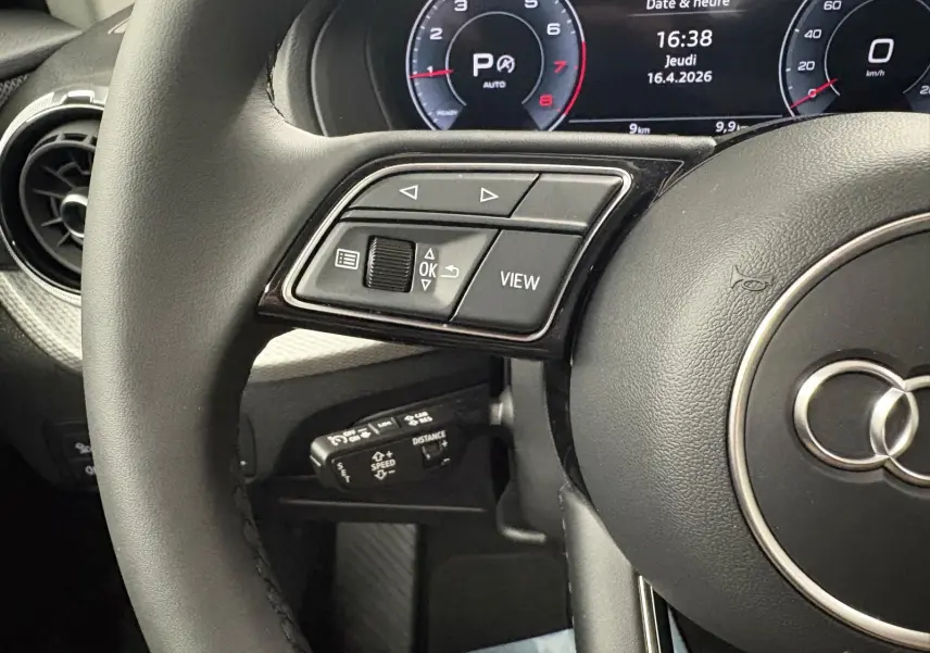 Gros plan sur le volant noir et le tableau de bord digital de l'Audi Q2 35 TFSI S Line 2026, affichant date et heure.