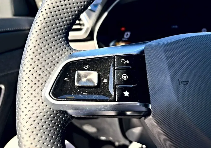Gros plan sur les commandes à gauche du volant perforé noir du MG Motor ZS 1.5 hybrid 197 standard 2026.