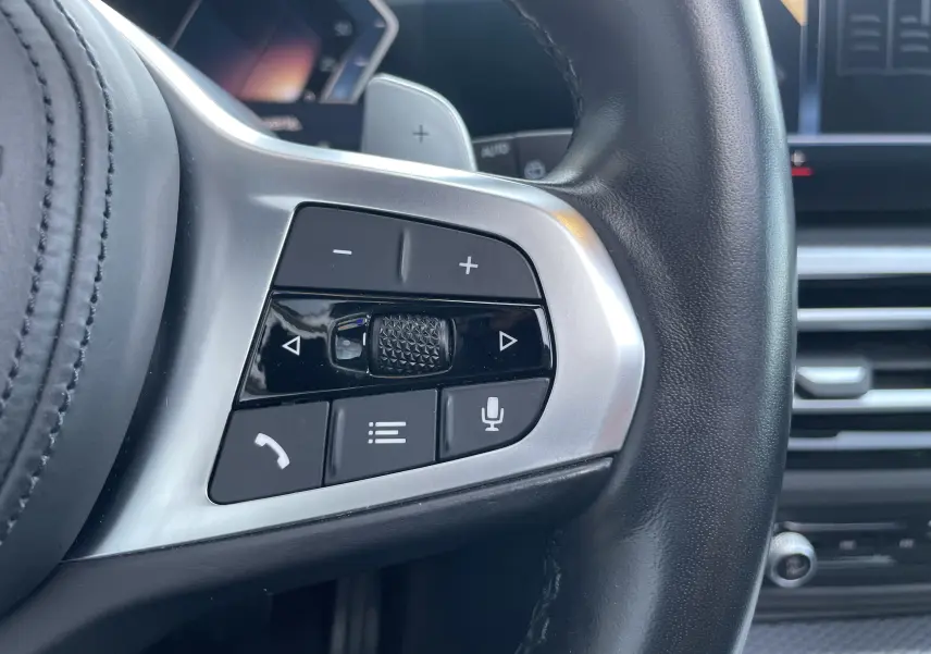 Gros plan sur les commandes multifonctions côté gauche du volant cuir noir d'une BMW Série 3 Touring G21 2022.