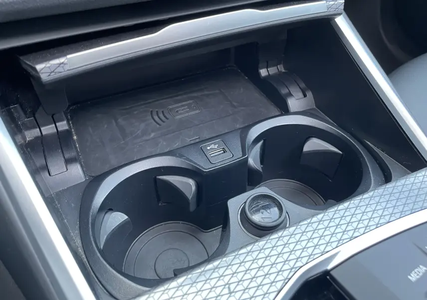Gros plan sur les porte-gobelets et la zone de recharge sans fil du BMW Série 3 Touring G21 noir métal, intérieur moderne.