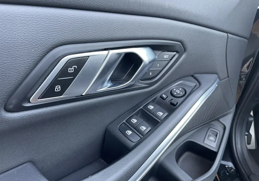 Détail de la porte avant gauche noire métal de la BMW Série 3 Touring G21 avec commandes de vitres et réglages mémoire des sièges.