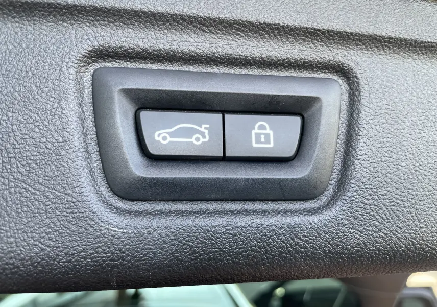 Boutons d'ouverture du coffre et de verrouillage intégrés dans le panneau intérieur d'une BMW Série 3 Touring G21 noire.