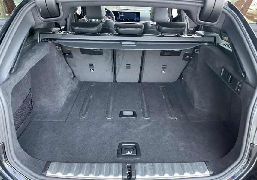 Coffre ouvert d'une BMW Série 3 Touring G21 noire métal, montrant l'espace de chargement et la banquette arrière rabattue partiellement.