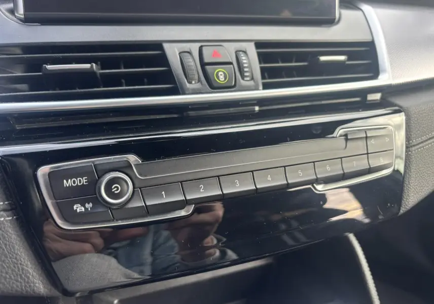 Détail de la console centrale noire brillante de la BMW Série 2 Active Tourer 218dA avec boutons de mode et mémoire radio.
