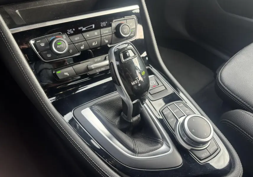 Gros plan sur la console centrale noire de la BMW Série 2 Active Tourer blanche, avec levier de vitesse automatique et commandes multimédia.