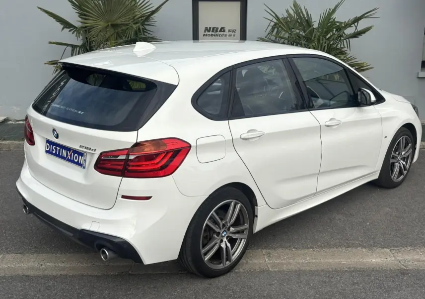 BMW Série 2 Active Tourer 218dA blanc vue 3/4 arrière droit avec jantes alliage 18 pouces et hayon électrique.
