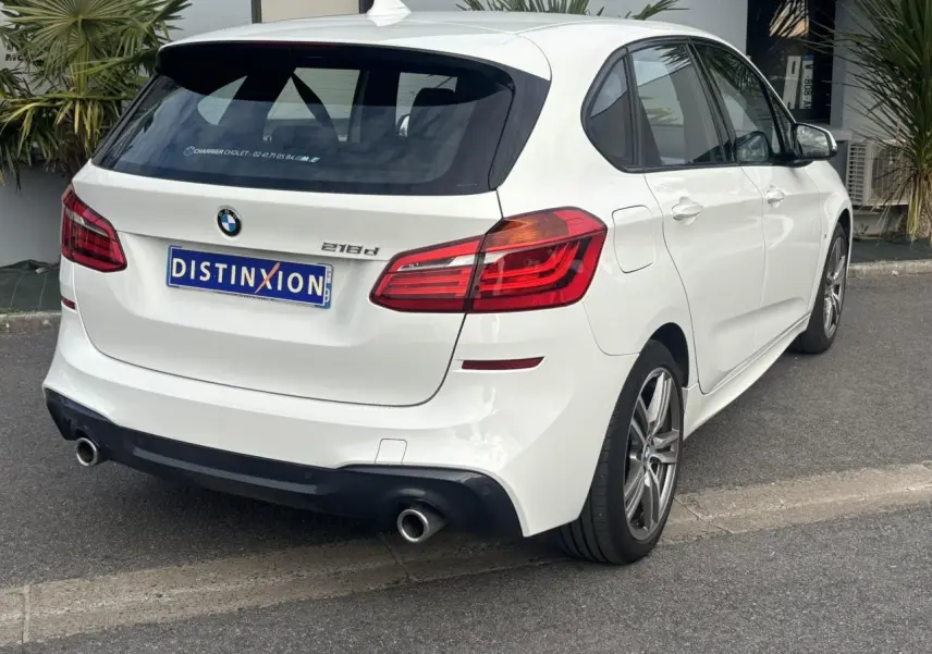 BMW Série 2 Active Tourer 218d blanc vue 3/4 arrière droit avec jantes alliage 18 pouces et double sortie d’échappement.