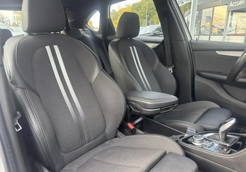 Vue intérieure côté avant droit de la BMW Série 2 Active Tourer 218dA M Sport, sièges noirs avec bandes grises et accoudoir central.