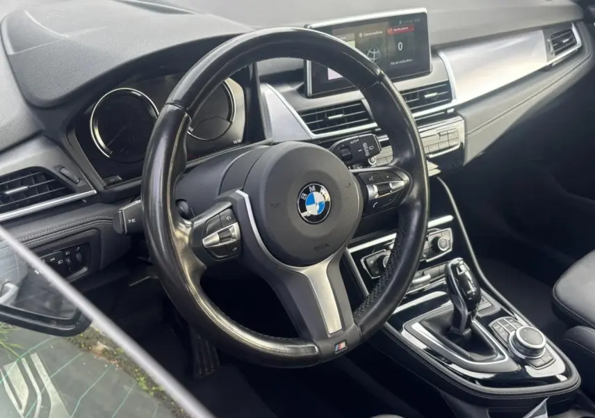Vue intérieure centrée sur le volant cuir M et la console centrale d’une BMW Série 2 Active Tourer blanche.