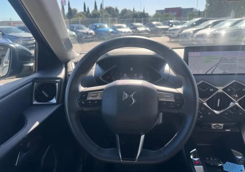 Vue intérieure centrée sur le volant DS d'une DS3 2024 gris, avec tableau de bord numérique et écran tactile de navigation.