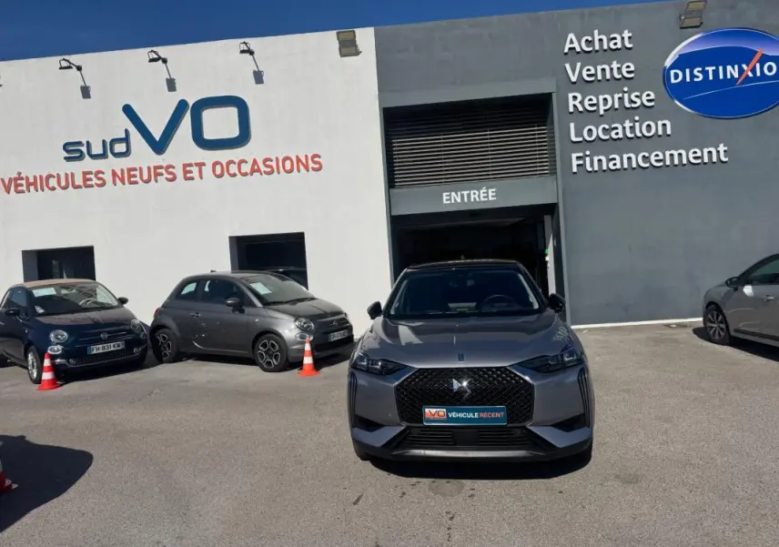 Vue avant d'une DS3 100 BVM6 Bastille gris 2024 avec calandre noire et jantes alliage 18 pouces, stationnée devant un garage.