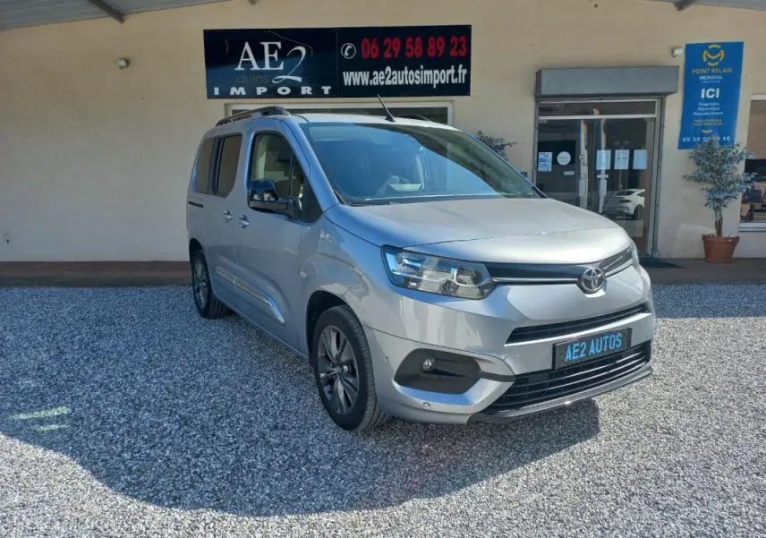 Toyota Proace City Verso gris vue 3/4 avant droit, avec calandre noire et jantes alliage, stationné devant un bâtiment.