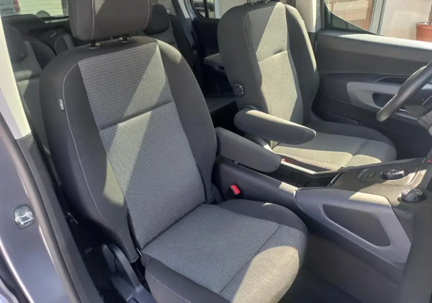 Vue intérieure côté conducteur du Toyota Proace City Verso gris 2023, sièges tissu avec accoudoirs et console centrale visible.