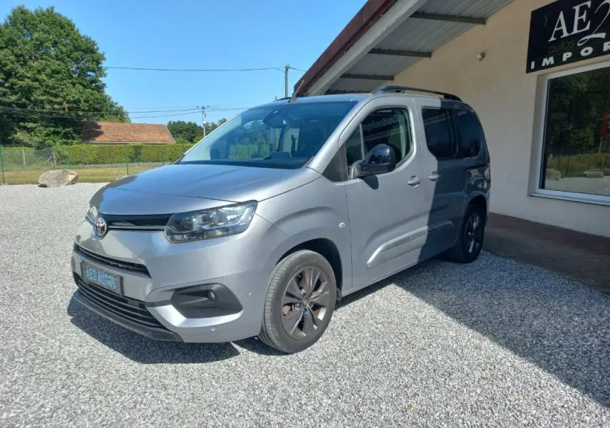 Toyota Proace City Verso gris, vue 3/4 avant droit, avec jantes foncées et toit équipé de barres de toit.