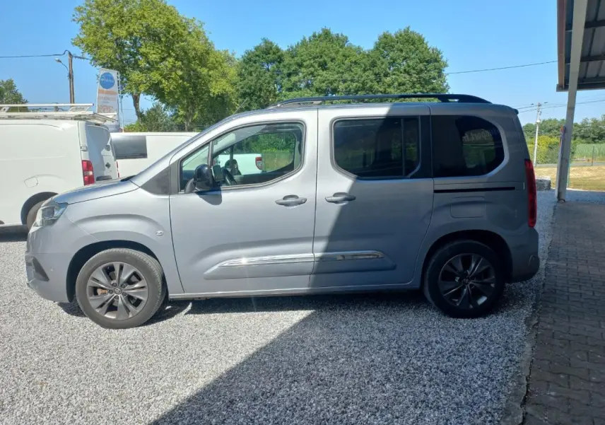 Vue de profil côté gauche d’un Toyota Proace City Verso gris 2023 garé sur un sol gravillonné, avec jantes foncées.