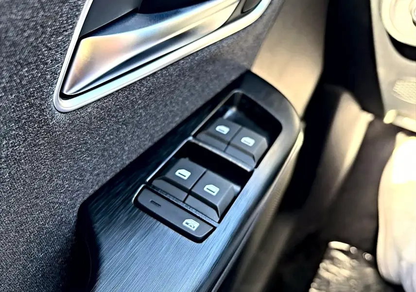 Gros plan sur la commande des vitres électriques côté conducteur du MG Motor ZS noir, avec poignée intérieure argentée.