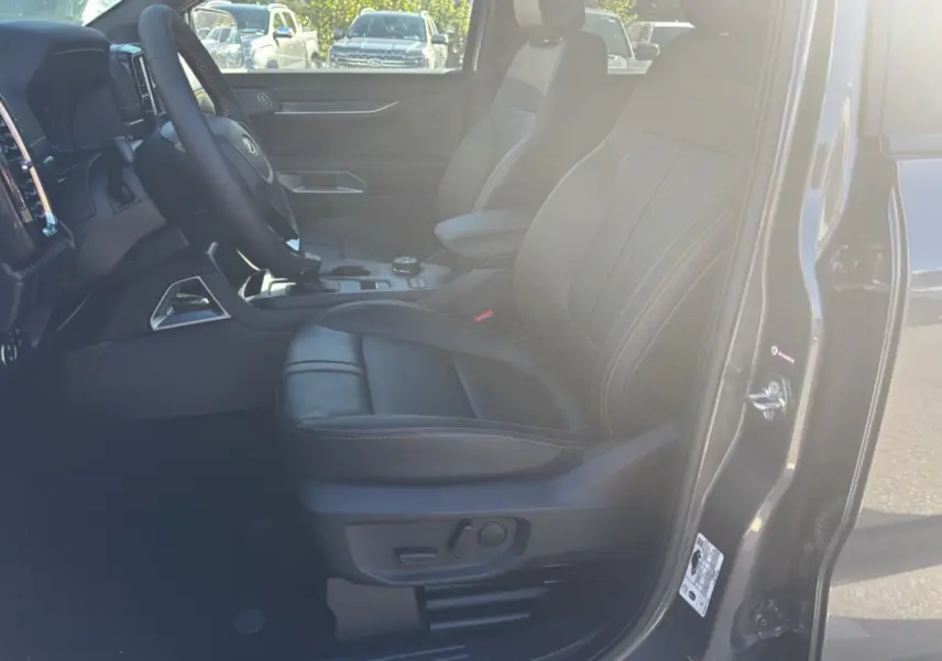 Vue intérieure côté conducteur du Ford Ranger gris carbone 2025, sièges cuir Wildtrak avec surpiqûres orange.