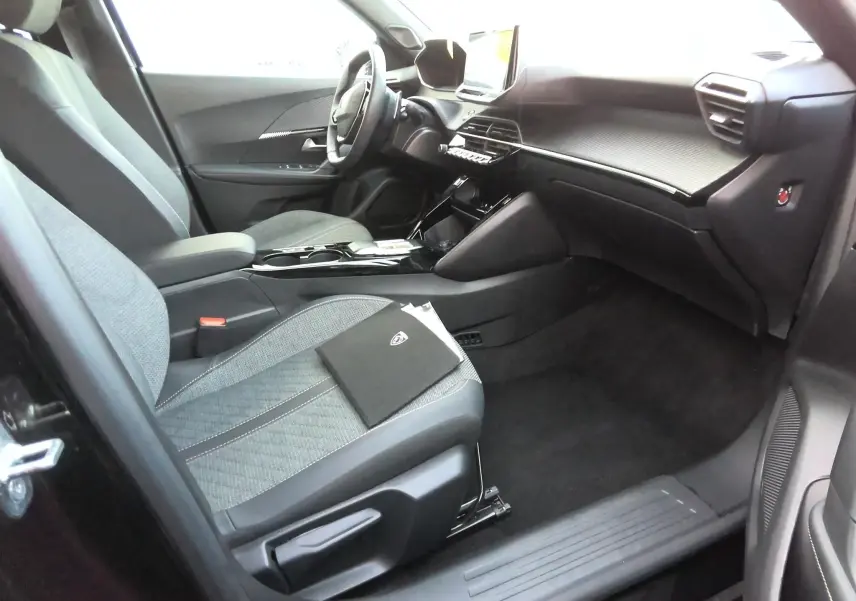 Vue intérieure côté conducteur du Peugeot 2008 noir 2025, montrant sièges tissu et tableau de bord moderne avec écran tactile.