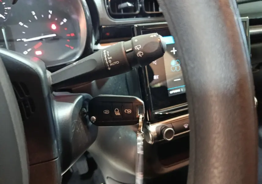 Gros plan intérieur sur la colonne de direction et le volant d’une Citroën C3 gris foncé avec clé insérée et tableau de bord tactile visible.